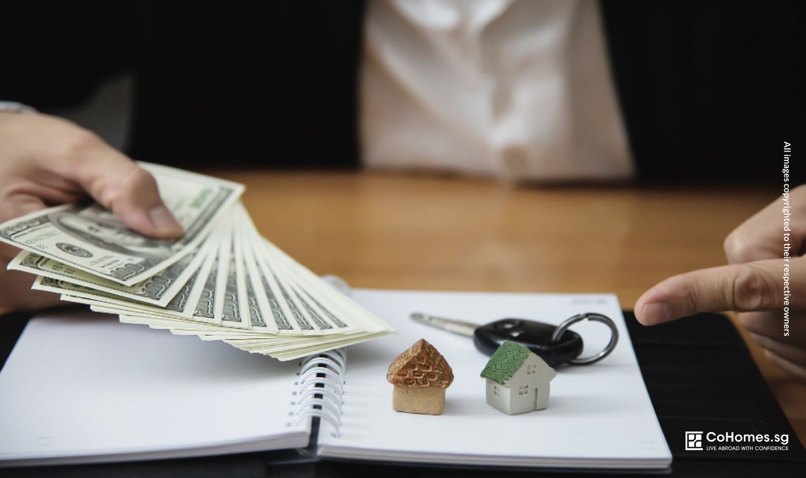 A property operator holding money with two miniature house models on a table